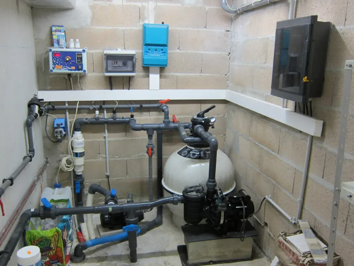Local technique de piscine avec filtre à sable, pompe, canalisations et appareils de régulation fixés au mur